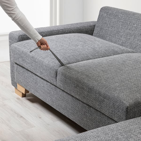 Person opens sofa beds storage compartment. Modern grey sofa converts into bed, wooden legs.