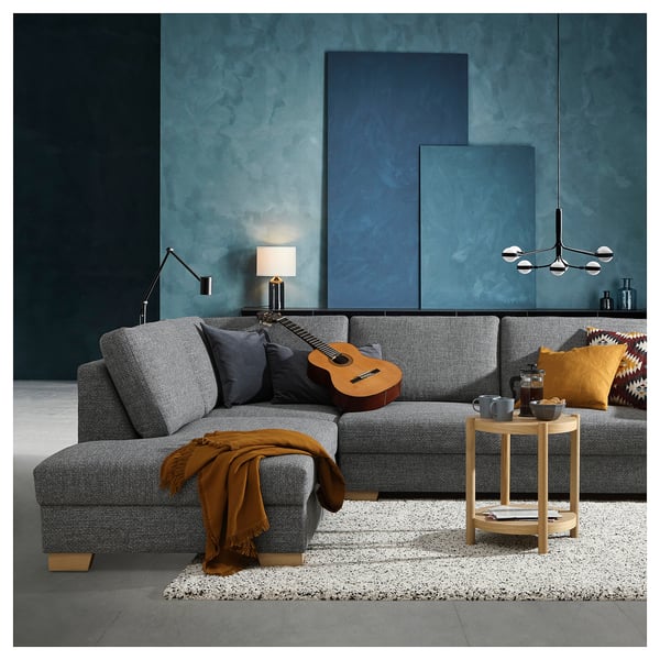 Modern living room with grey SÖRVALLEN sofa, orange throw, guitar, wooden side table, colourful pillows, and blue-green wall.