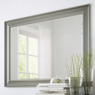 Large mirror with vertical & horizontal hang options, reflective surface, with safety film. Shown on wall reflecting window, next to plants & books.