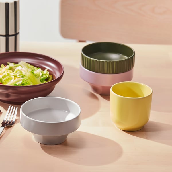 Colourful bowls on a table. One holds salad, others are empty.