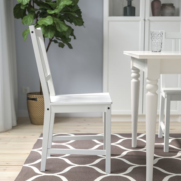 A white wooden chair with a high back, placed near a small table with a patterned rug underneath.