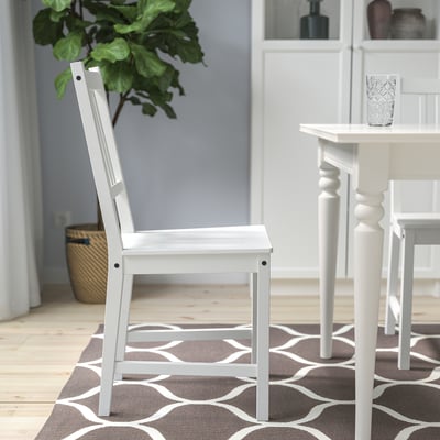 A white wooden chair with a high back, placed near a small table with a patterned rug underneath.