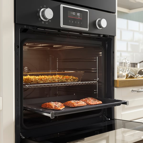 Black oven with digital display baking salmon and casserole. True fan, top/bottom heating, multiple racks.