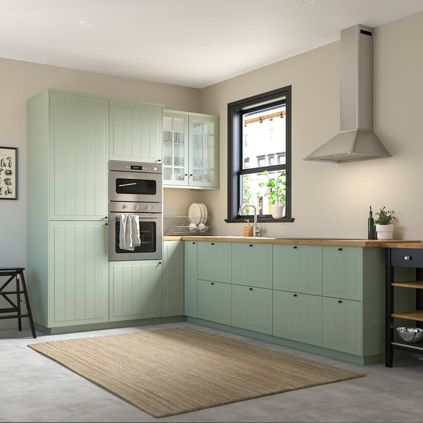 Modern, green STENSUND kitchen set with tall cabinets, rail, and integrated oven. Light, wooden countertops and a neutral floor rug.