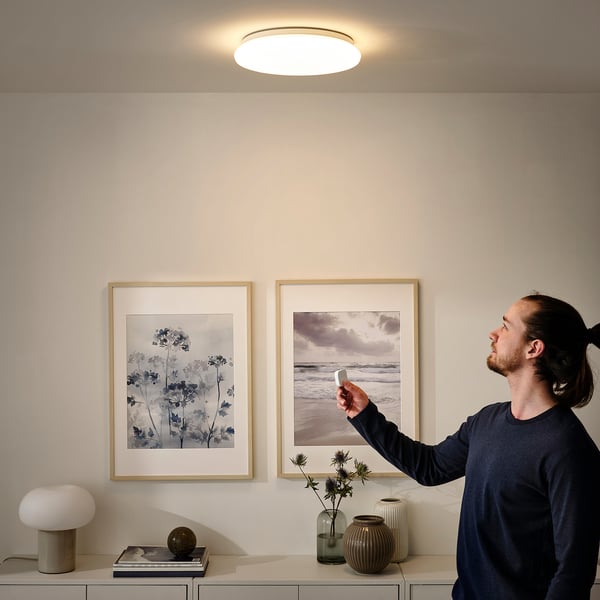 Person adjusts wireless dimmer for a large ceiling light in a modern room with art and decor.