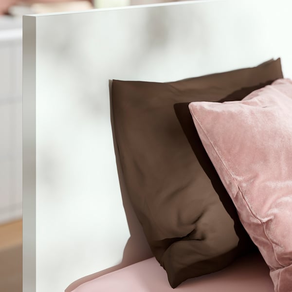 Close-up of a modern bed with a sturdy, white headboard and neatly arranged pillows in muted tones, showcasing high-quality design and comfort.