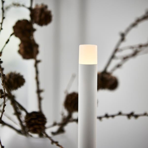 Modern white led candle in clear focus, surrounded by soft, out-of-focus branches.