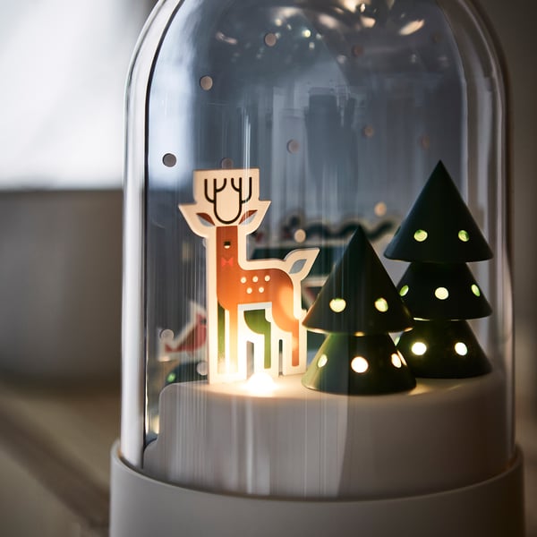 Snow globe lamp with deer and trees, warmly lit, sitting on a table.