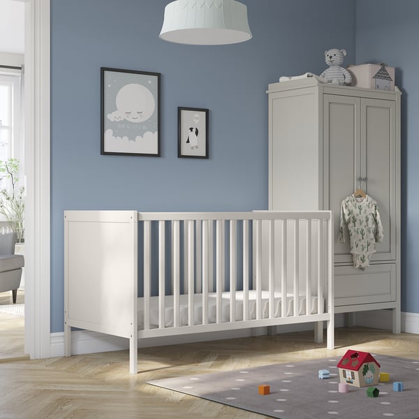 SUNDVIK white baby cot near grey wardrobe, blue wall with toys and posters.