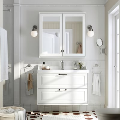 TÄNNFORSEN bathroom: white vanity, mirror cabinet, patterned tiles. Sink flanked by wall lights, towels on silver rings, geometric tile floor.