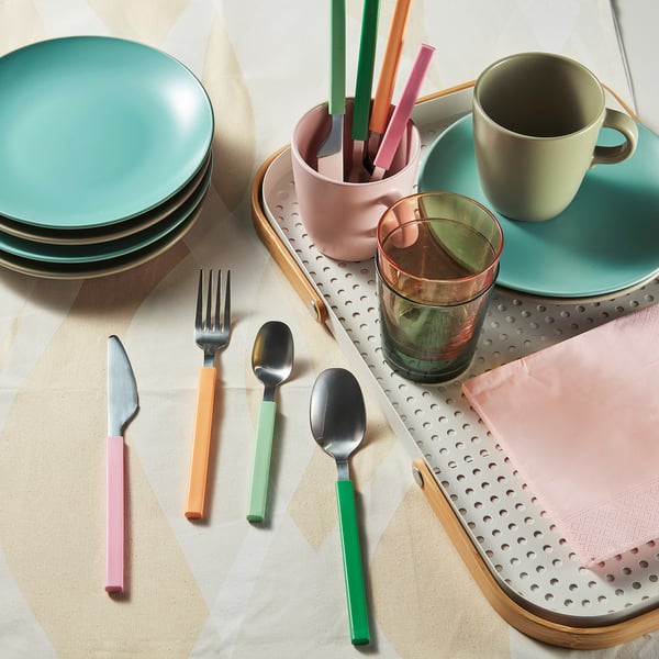Colourful cutlery set on a perforated tray, with plates, cups, and glasses. Forks, knives, spoons, and teaspoons are neatly arranged, ready for use.