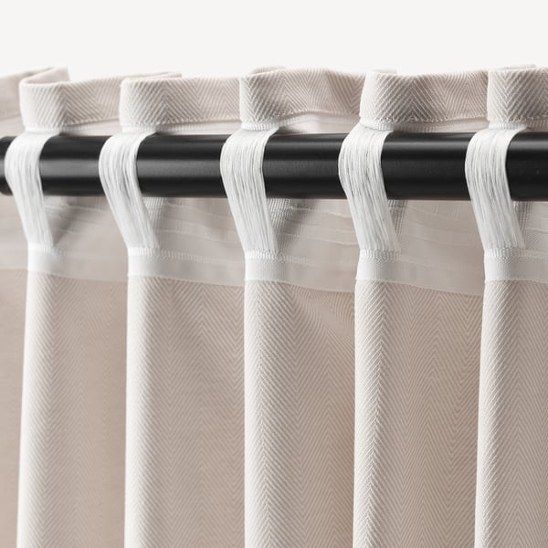 Close-up of white curtains with herringbone pattern hanging from black rod, attached via loops.