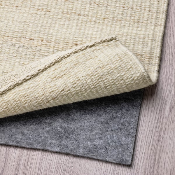 A rolled-up beige wool rug lies on a light wooden floor, showcasing its thick, textured surface.