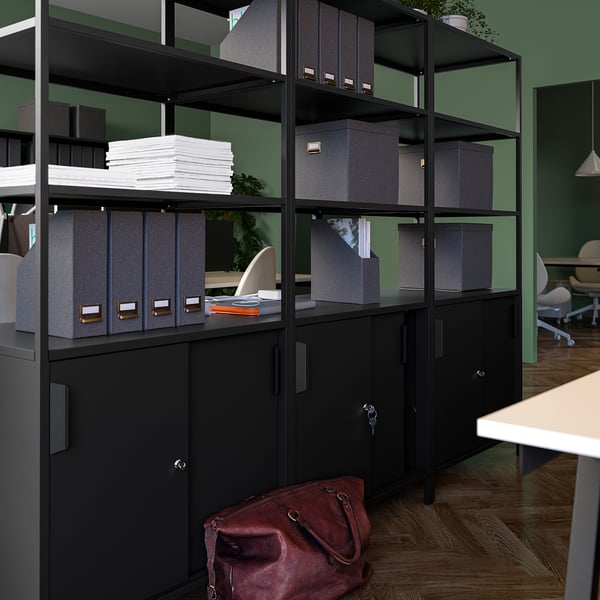 A TROTTEN black double-sided office cabinet with open and closed storage, wooden floor, and green walls.