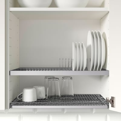 Open wall cabinet with dishes stored in a draining rack, below are glasses and mugs on a wire rack, set in a clean, white kitchen.