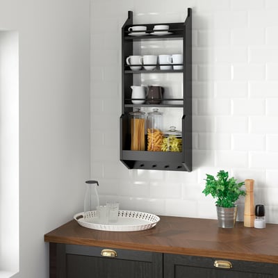 Modern kitchen with black VADHOLMA shelf holding cups & jars on white subway tiles above dark wood countertop with tray and plant.