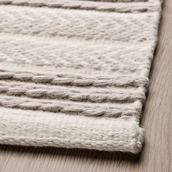 Handwoven grey and cream rug on wooden floor, showcasing intricate wool texture and craftsmanship.