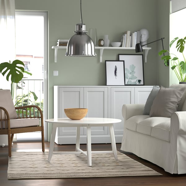 Cosy living room with green walls, white chair, round table, and large traditional rug.