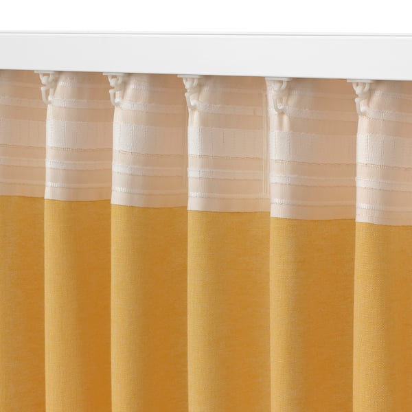 A close-up of textured curtains with a yellow and beige colour scheme, hanging neatly with a white curtain rod and hooks.