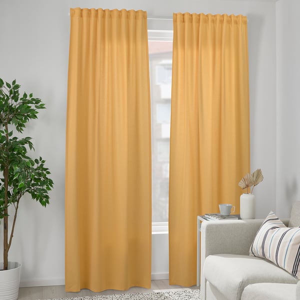 Modern living room with large mustard yellow VÄXELBRUK curtains, white couch, and plant. Light-blocking, recycled fabric.