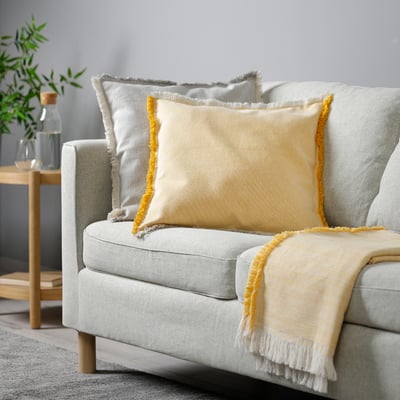 Light grey sofa with large yellow-fringed pillows.