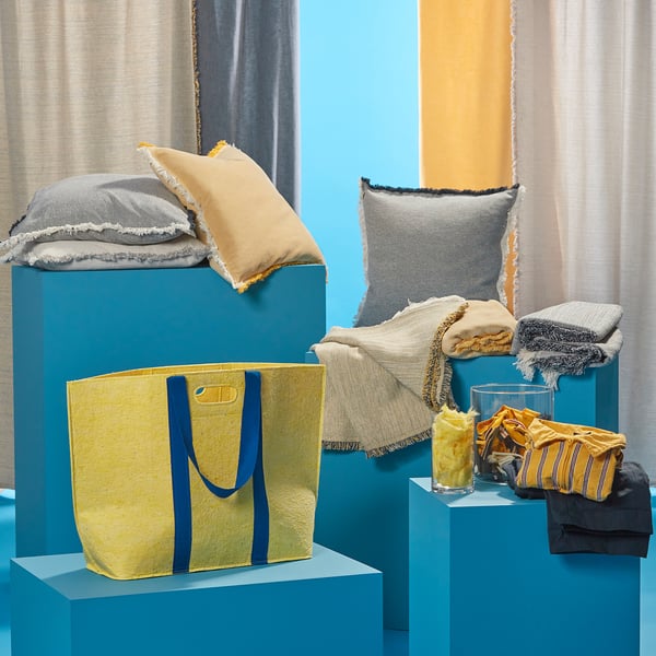 VÄXELBRUK yellow bag, grey pillows, blue pedestals. Recycled fabric blend. Bag is large, pillows are square.