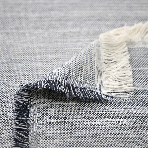 Textured, woven throw with fringes, featuring light and dark shades. High-quality, recycled fibres, visible in intricate weave.