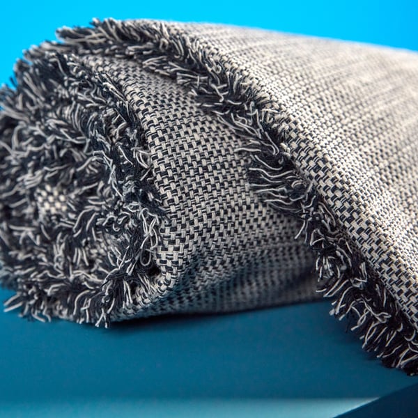 Folded grey throw with fringe on teal background. Soft, recycled fabric with varied texture.