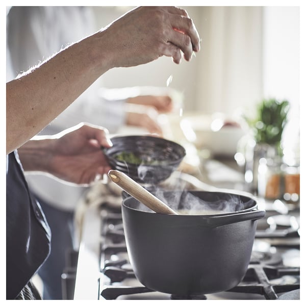 Chef seasoning cast iron pan, VARDAGEN, black, on stove.