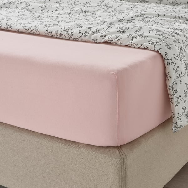 Light pink fitted sheet over beige bedskirt with black vine print bedspread.