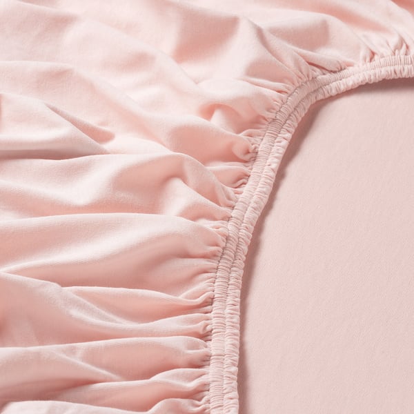 Close-up of light pink cotton jersey fabric, showing soft texture and elastic edging detail.