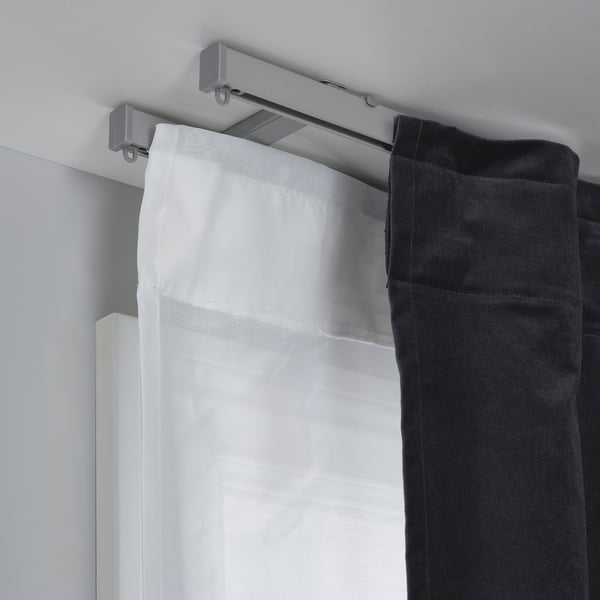 A curtain holder with a metallic track, supporting white sheer and black panel curtains. Its part of the VIDGA system for easy curtain changes.