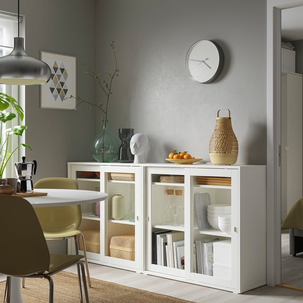 Modern dining area with white VIHALS cabinet, glass doors, and sleek design, fitting between chairs and near a grey wall.