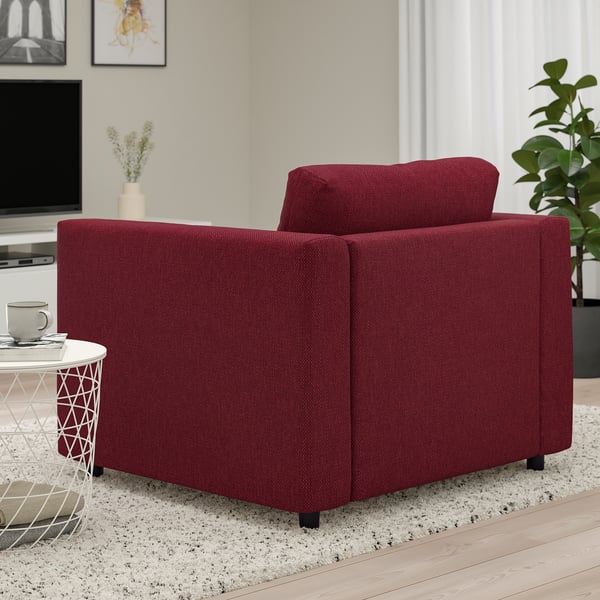 Modern red armchair in living room near side table with mug and remote.