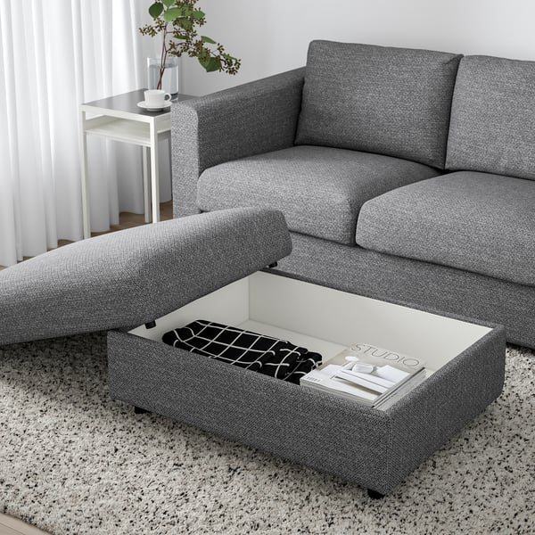 Modern living room with a grey VIMLE sofa and ottoman. The ottoman has a liftable seat revealing storage space with books and a remote control inside.