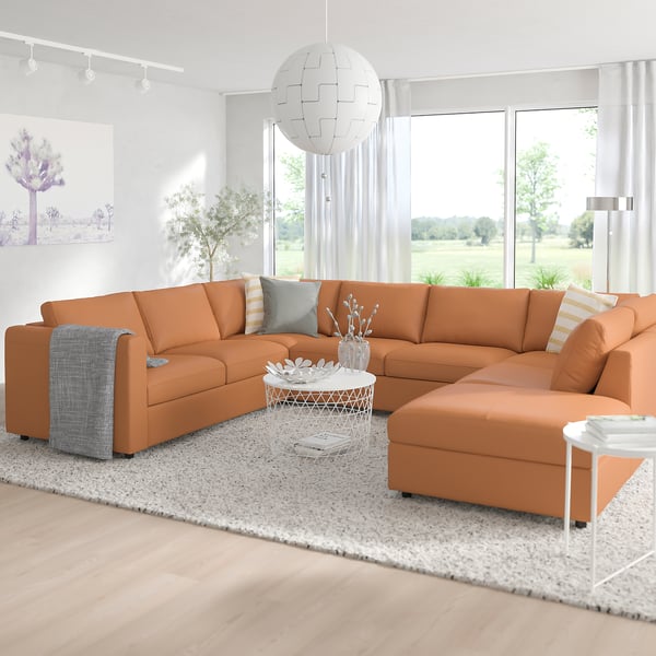 Modern orange l-shaped VIMLE sofa with cushions, centred in a bright, minimalist living room. Large window, white curtains, rug, and coffee table.