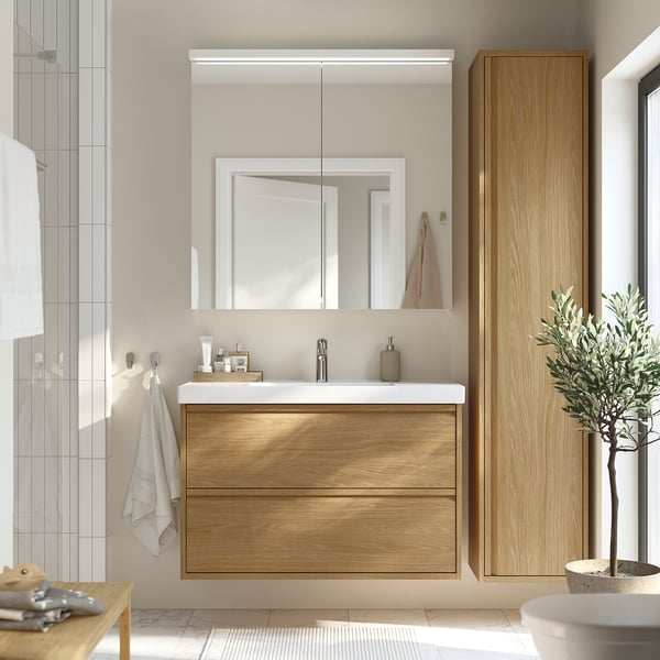 Moderne badeværelse med ÄNGSJÖN egetræsvask, spejl, greb og minimalistisk vask. Lodret opbevaring og indretningsgrønt.