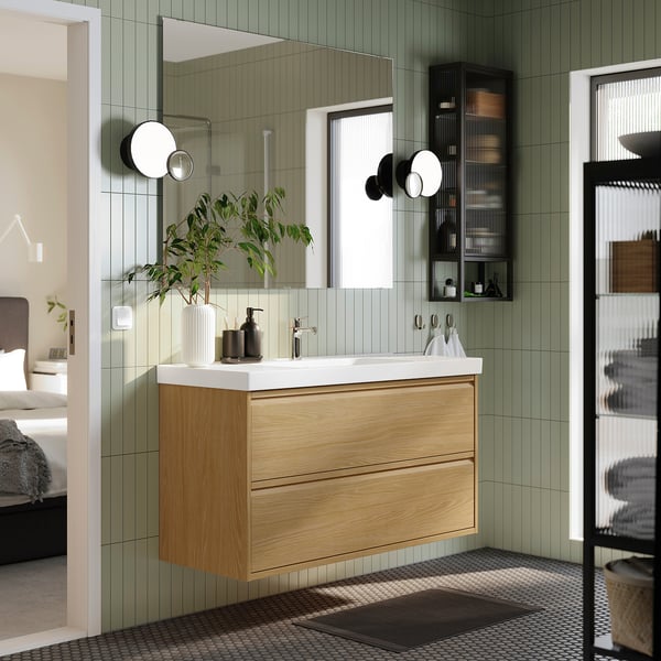 Moderne badeværelse med egetræsbord, spejl, planter og glashylder. ÄNGSJÖN-serien blander træ og minimalistisk design.