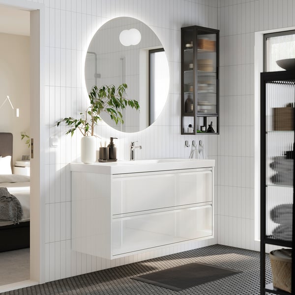 Moderne badeværelsesscene: hvid ÄNGSJÖN forfængelighed, rundt spejl, sort tilbehør, plante. Pladsbesparende design.