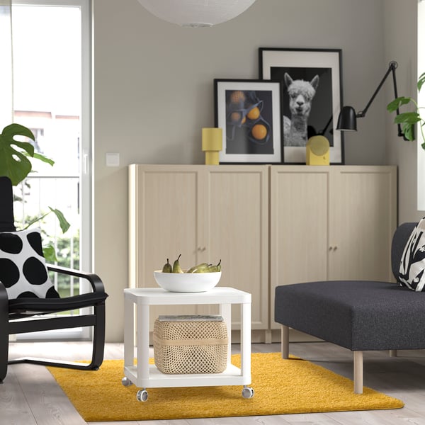 Moderne stue med gult tæppe, træskab, sort stol, grå sofa og hvidt sidebord.