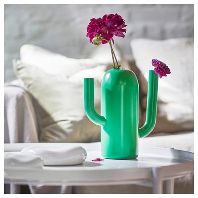 Lysegrøn kaktusformet vandkande vase med lyserøde blomster på bordet, moderne design.