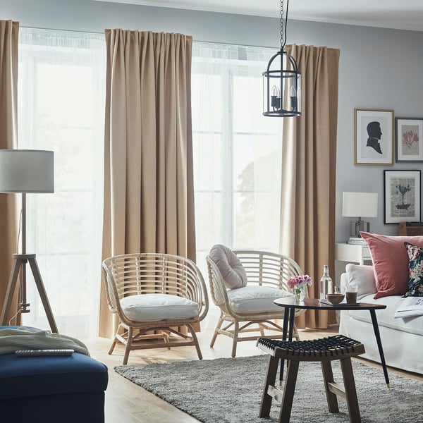 Stue med beige gardiner, kurvestole og træbord.