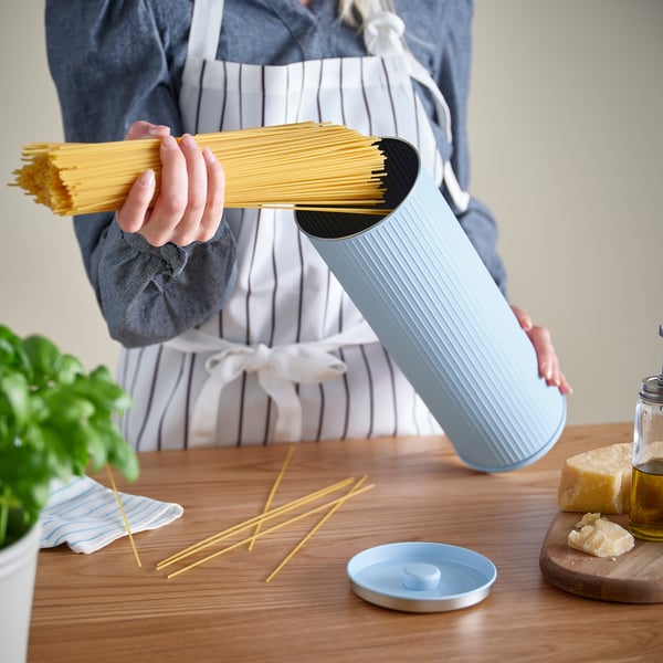 Person med lyseblå BETTHAJ-enhed med spaghetti indeni, der viser køkkenscene.