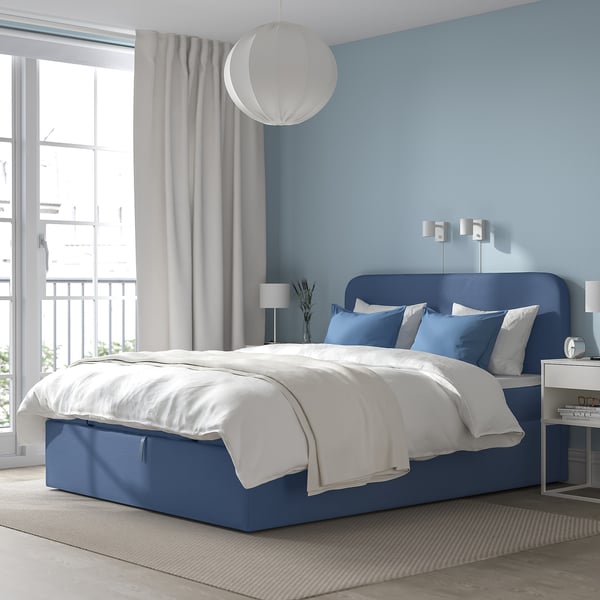 Moderne soveværelse med BLÅFJÄLLET blå divan, hvidt sengetøj, stort vindue, lampe, blå væg og grå gardiner.