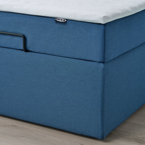 En blå osmannisk divanseng med integreret opbevaring; Et nærbillede af basen og en løftestrop for nem adgang.