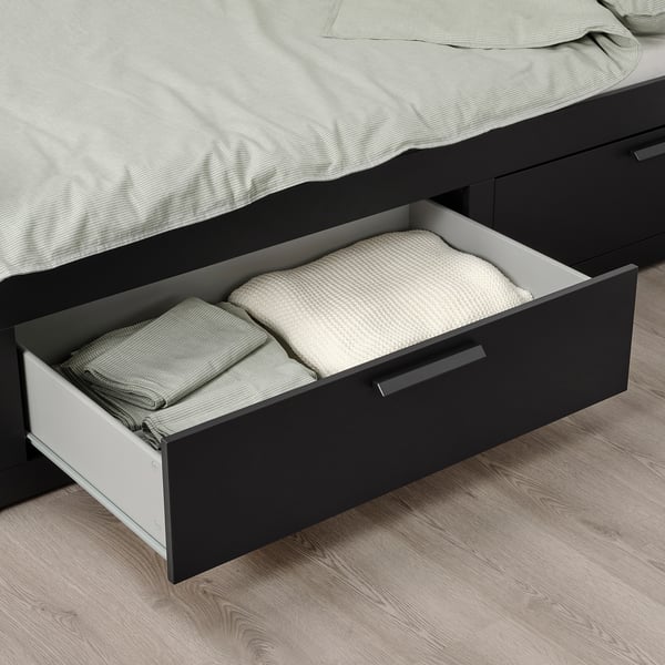 Åben skuffe af sort BRIMNES daybed fyldt med foldede tæpper og puder.