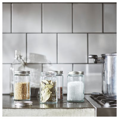Tre CITRONHAJ krydderiglas i klart glas med metallåg, fyldt med korn, laurbærblade og salt, pænt arrangeret på en bordplade.