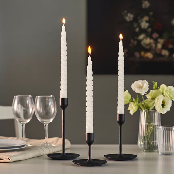 Tre tændte spirallys i sorte holdere på et bord med glas og blomster.