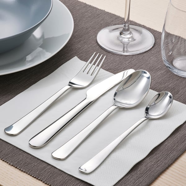 Borddækning med gaffel, kniv og skeer på grå serviet, tallerken og glas.