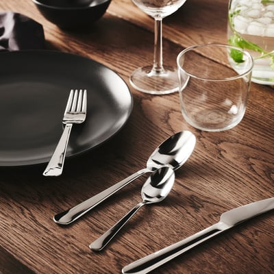 Rustfrit bestik, glas, sort tallerken på et mørkt bord.